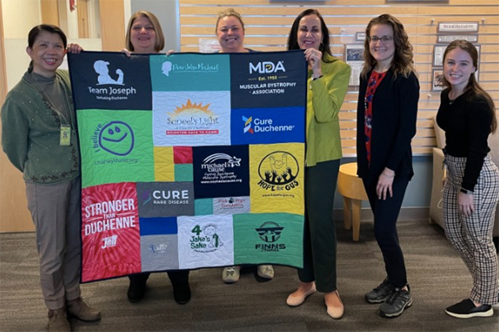 Group of people holding up a patchwork quilt.